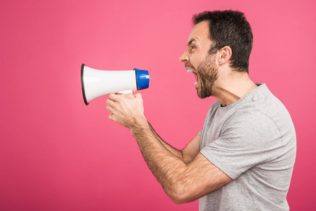 aggressive man shouting with megaphone, isolated on pinkの写真素材