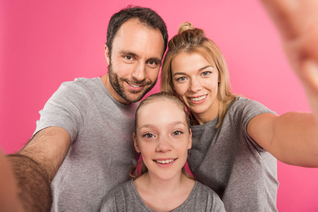 smiling family taking selfie together, isolated on pinkの写真素材