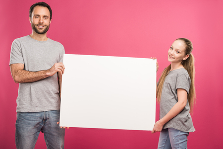 father and adorable daughter posing with empty board, isolated on pinkの写真素材