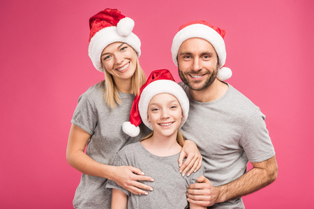 portrait of smiling family with daughter in santa hats, isolated on pinkの写真素材