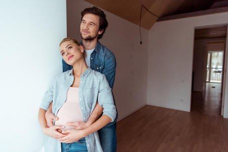 thoughtful man embracing pregnant wife in apartmentの写真素材