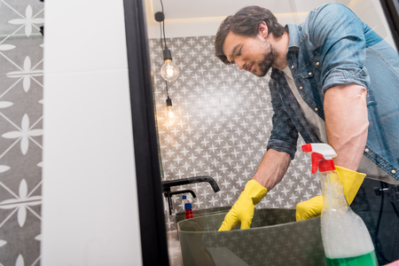 mirror reflection of handsome man in rubber gloves cleaning sink in bathroomの写真素材