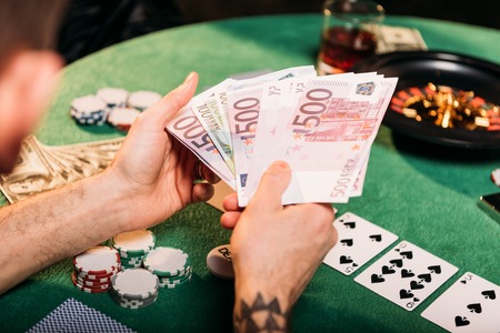 cropped image of tattooed man holding euro banknotes at poker table in casinoの写真素材