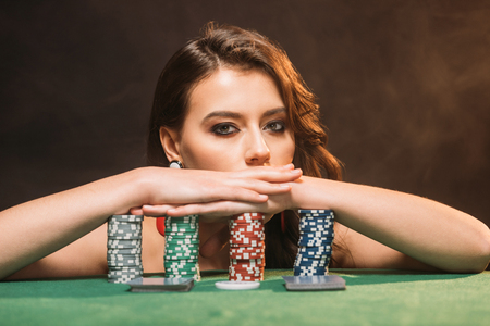 beautiful brown haired girl leaning on poker chips and looking at camera isolated on blackの写真素材