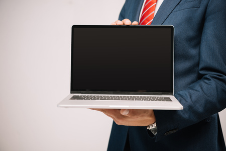 cropped view of businessman in suit presenting laptop with blank screen isolated on greyの写真素材