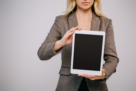 cropped view on businesswoman in suit presenting digital tablet with blank screen isolated on greyの写真素材