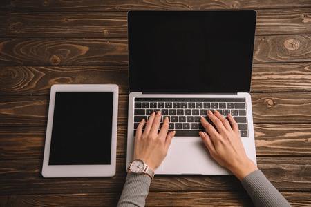 cropped view of woman typing on laptop at workplace with digital tabletの写真素材