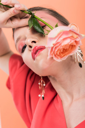 portrait of beautiful stylish girl holding rose and posing isolated on living coralの写真素材