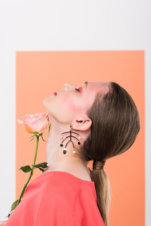 beautiful stylish girl holding rose and posing with eyes closed and living coral on backgroundの写真素材