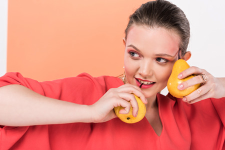 beautiful fashionable girl holding pears, looking away and posing with living coral on backgroundの写真素材