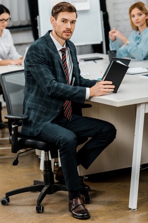 young businessman with notebook sitting at workplace in officeの写真素材