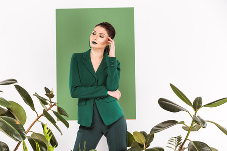 beautiful stylish woman looking away while posing with plants and sea green on backgroundの写真素材