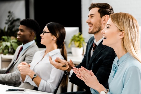 smiling multiracial businesspeople applauding to speaker in officeの写真素材