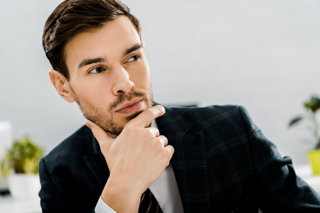 portrait of thoughtful businessman in suit looking away in officeの写真素材