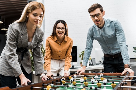 cheerful business colleagues playing table football together in office