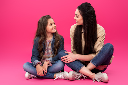 full length view of smiling mother and daughter sitting and talking on pinkの写真素材