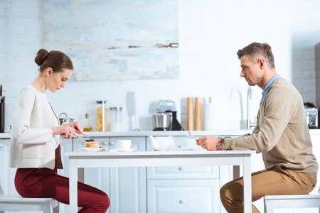 selective focus of dissatisfied adult couple during breakfast in kitchenの写真素材