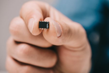 selective focus of man holding black, metallic microchipの写真素材