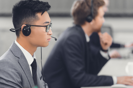 side view of focused young asian businessman in headset working with colleagues in officeの写真素材
