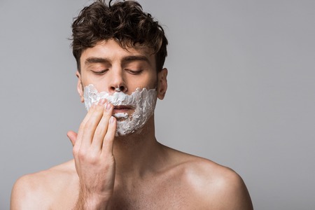 handsome man applying shaving foam on face, isolated on greyの写真素材