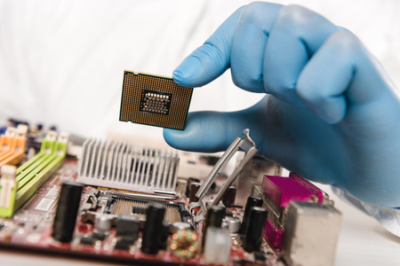 cropped view of microchip in hand of scientist near motherboardの写真素材