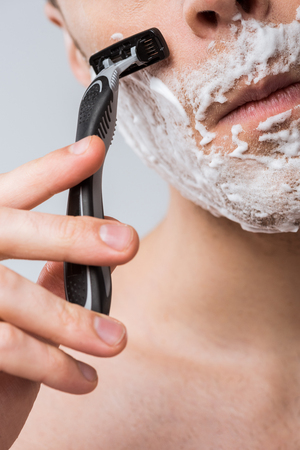 cropped view of young man foam on face shaving with razor, isolated on greyの写真素材