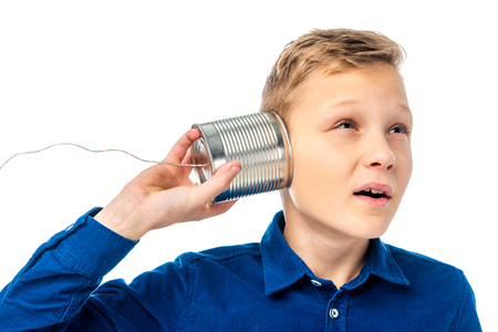 smiling boy holding tin with rope near ear and listening isolated on whiteの写真素材