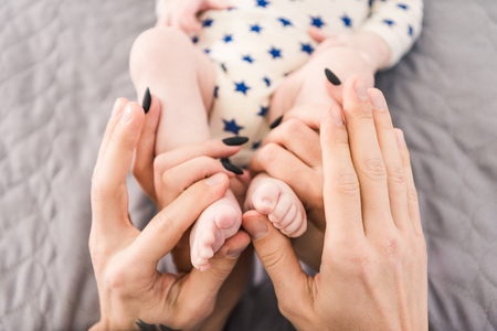 partial view of parents holding little babys feet in hands togetherの写真素材