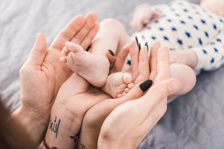 partial view of parents holding little babys feet in hands togetherの写真素材