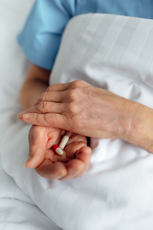 cropped view of senior woman lying in bed and holding pills in hospitalの写真素材