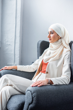 young muslim woman sitting in chair and looking awayの写真素材