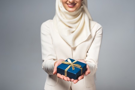 cropped shot of smiling young muslim woman holding gift box isolated on greyの写真素材