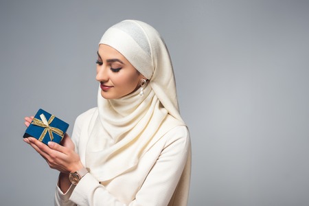 smiling young young muslim woman holding present isolated on greyの写真素材