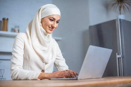 smiling young muslim woman using laptop at homeの写真素材