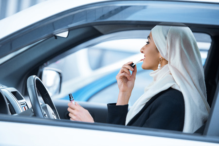 young muslim woman sitting in car and applying makeupの写真素材