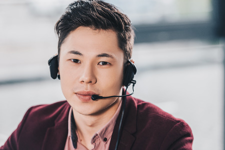 handsome young asian manager in headset looking at camera in officeの写真素材