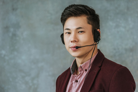 handsome young asian call center operator looking at camera on greyの写真素材