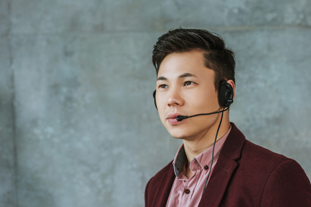 handsome young asian call center operator looking away on greyの写真素材