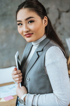 beautiful young asian businesswoman holding digital tablet and smiling at cameraの写真素材