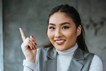 beautiful kazakh businesswoman pointing up with finger and smiling at cameraの写真素材