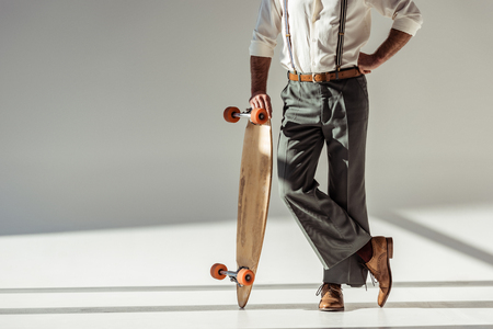 cropped view of stylish man holding longboard on grey backgroundの写真素材