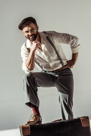 handsome bearded man near retro suitcase smiling and looking at camera on grey backgroundの写真素材