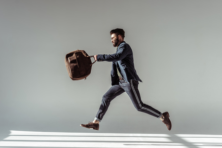 handsome bearded man with brown bag jumping on grey backgroundの写真素材