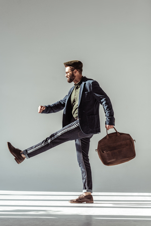 handsome bearded man in cap with brown bag marching on grey backgroundの写真素材