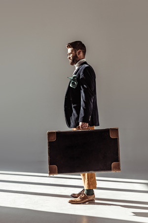 side view of handsome bearded man in glasses holding vintage suitcaseの写真素材