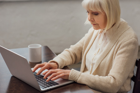 senior woman sitting at table and typing on laptop at homeの写真素材