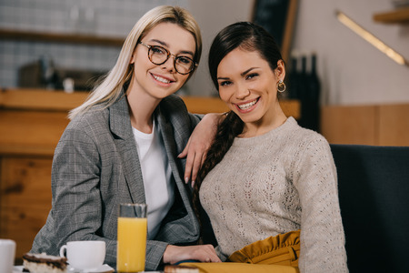 cheerful woman sitting with friend in glasses in cafeの写真素材