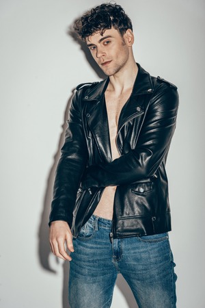 stylish sexy man posing in jeans and black leather jacket on greyの写真素材