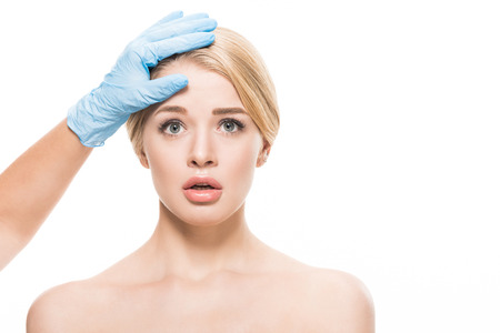 cosmetologist touching forehead of scared young woman looking at camera isolated on white