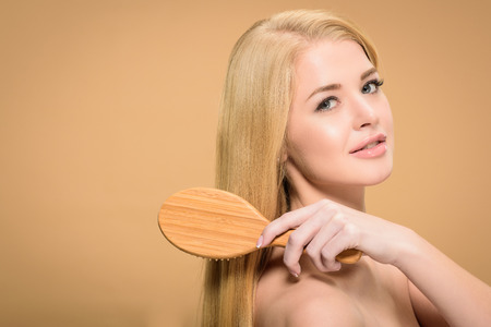 Attractive young woman looking at camera while brushing straight hairの写真素材